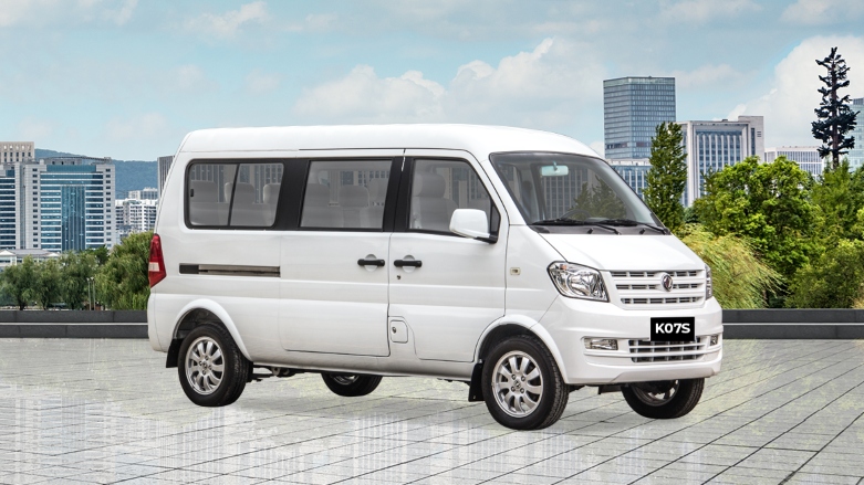 Vista delantera lateral de van de turismo DFSK K07S color blanca estacionada con vistas a la ciudad.